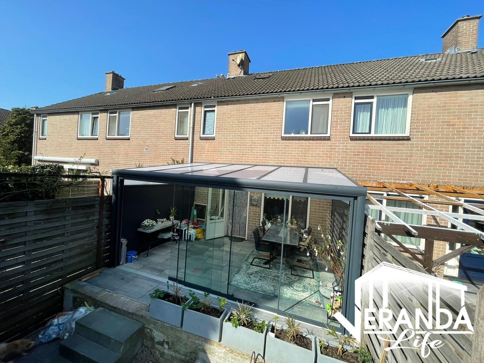 Een bakstenen huis met een groot, met glas overdekt terras ervoor.