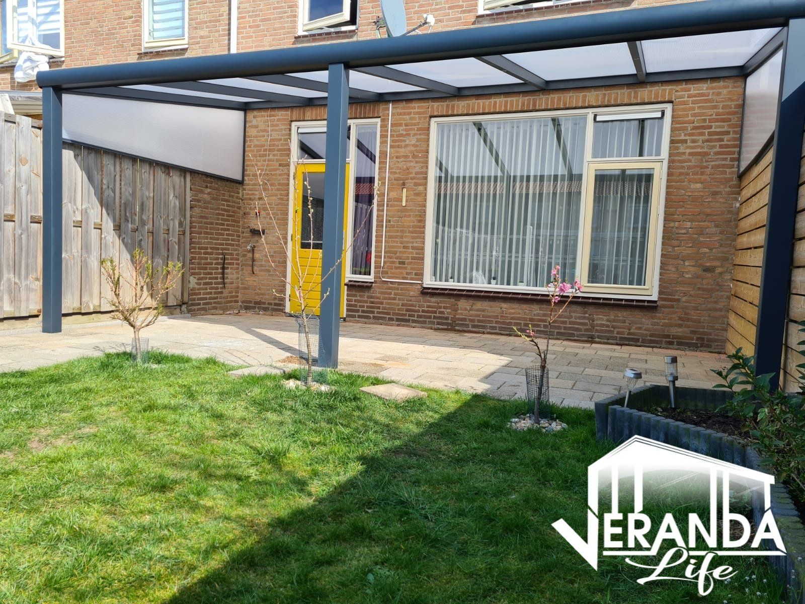 Een huis met een overdekt terras in de achtertuin.