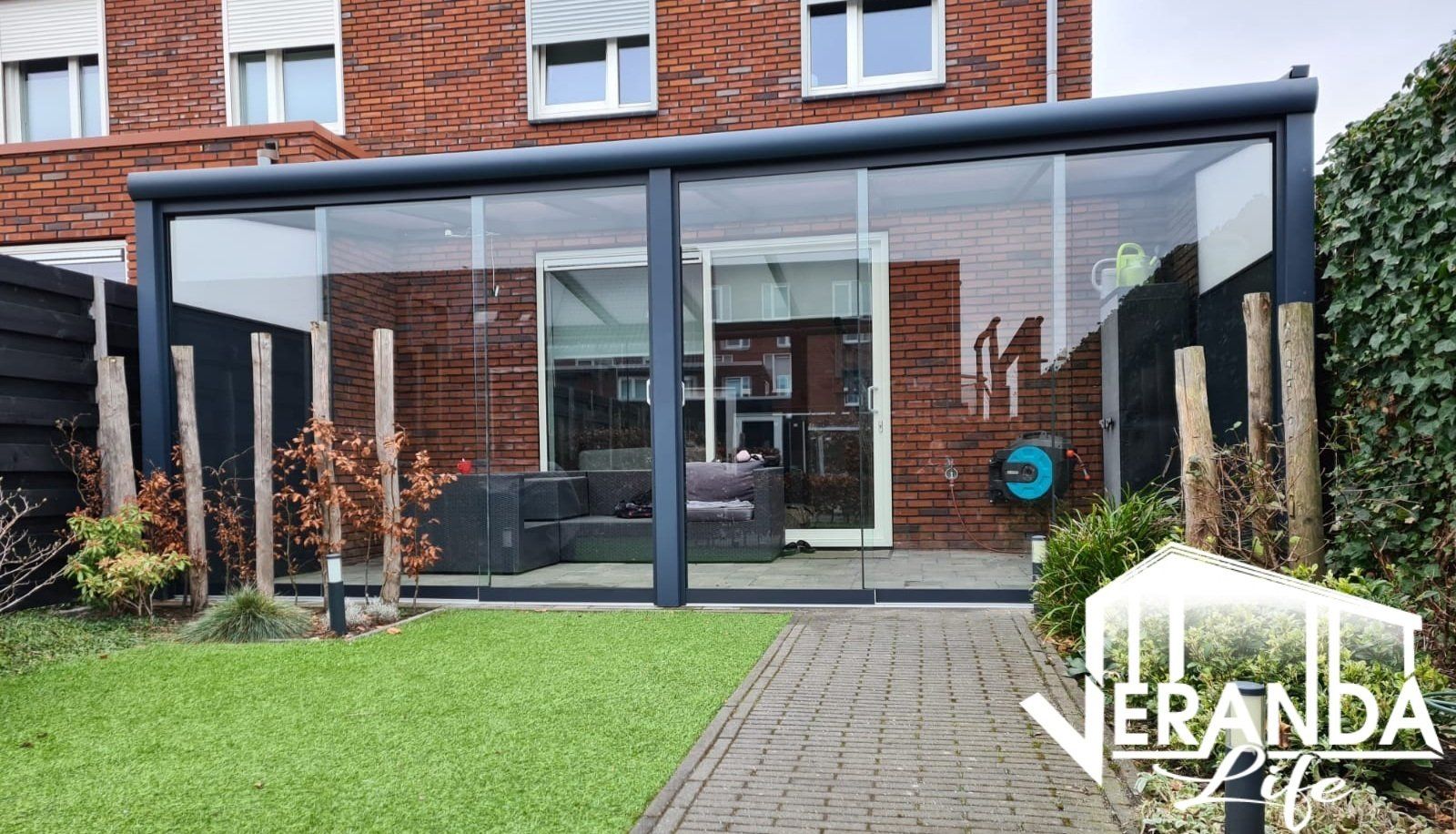 Een bakstenen huis met een glazen overdekt terras in de achtertuin.