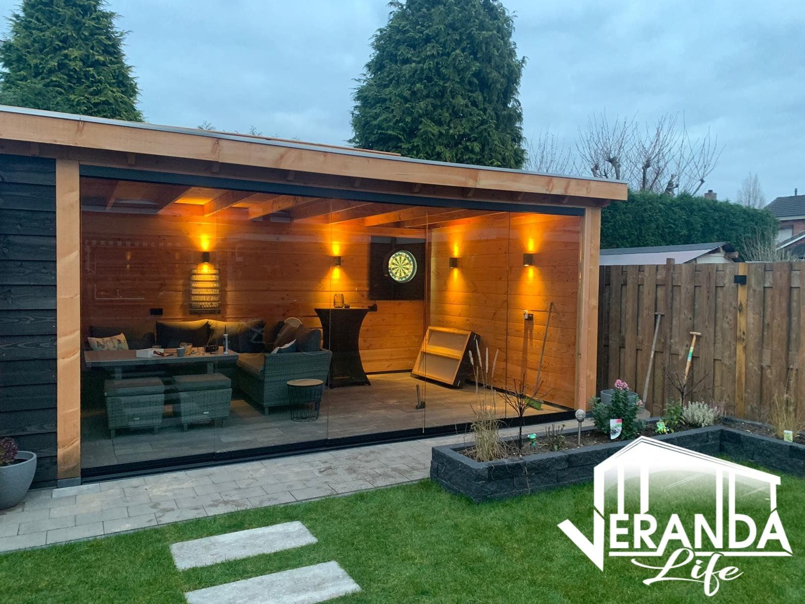 Een houten schuurtje met een bank, tafel, stoelen en een klok aan de muur.