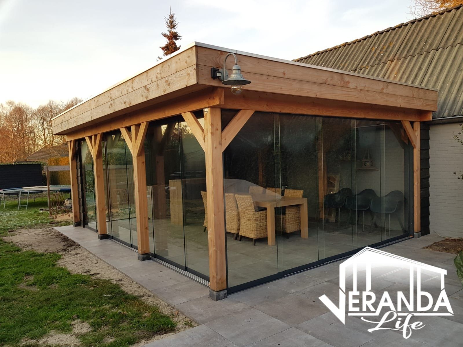 Een houten tuinhuisje met glazen schuifdeuren en een tafel en stoelen.