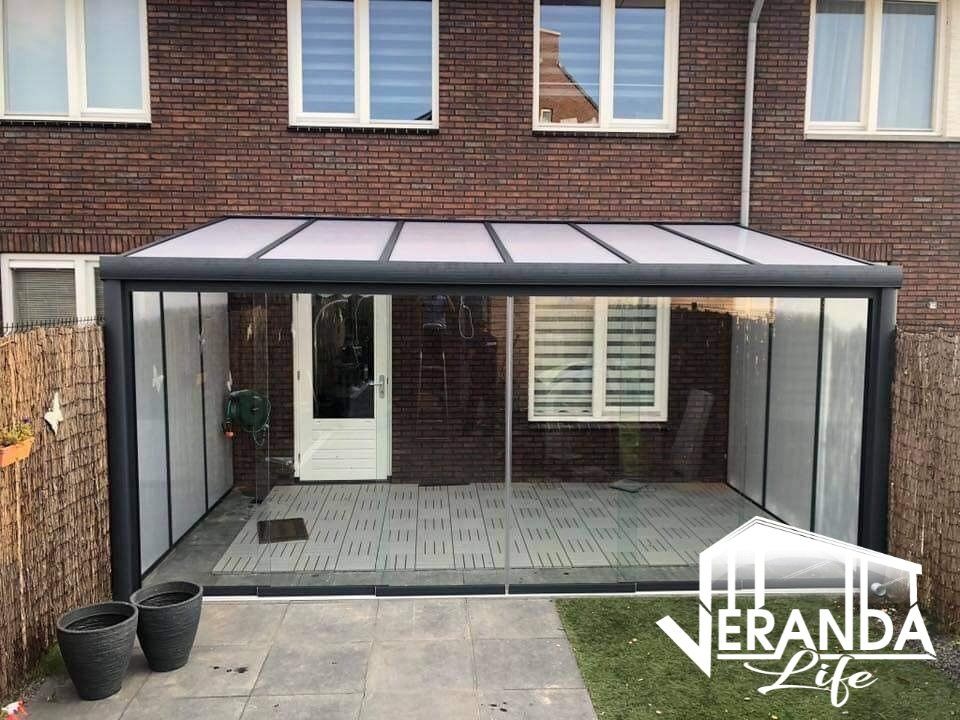 Een patio met een dak en glazen schuifdeuren voor een bakstenen huis.