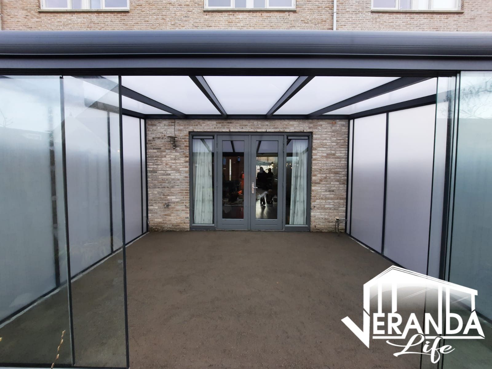 Een veranda met glazen schuifdeuren en een bakstenen gebouw op de achtergrond