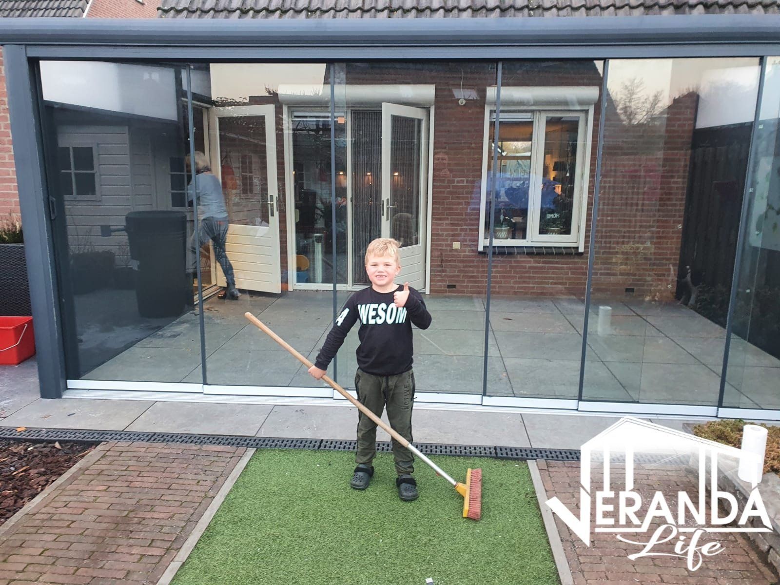 Een jonge jongen veegt het gras voor een huis.