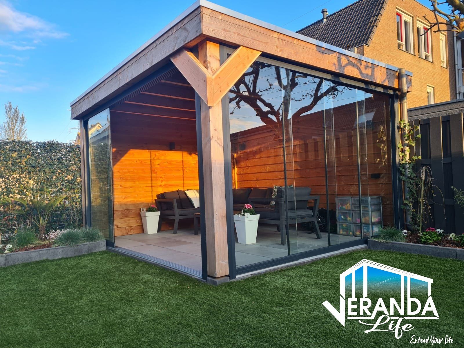 Een houten tuinhuisje met glazen schuifdeuren in een achtertuin.