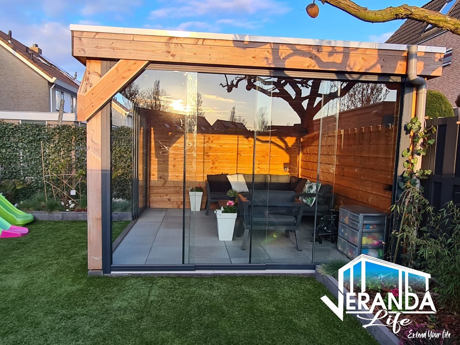 Een houten tuinhuisje met glazen schuifdeuren in een achtertuin.