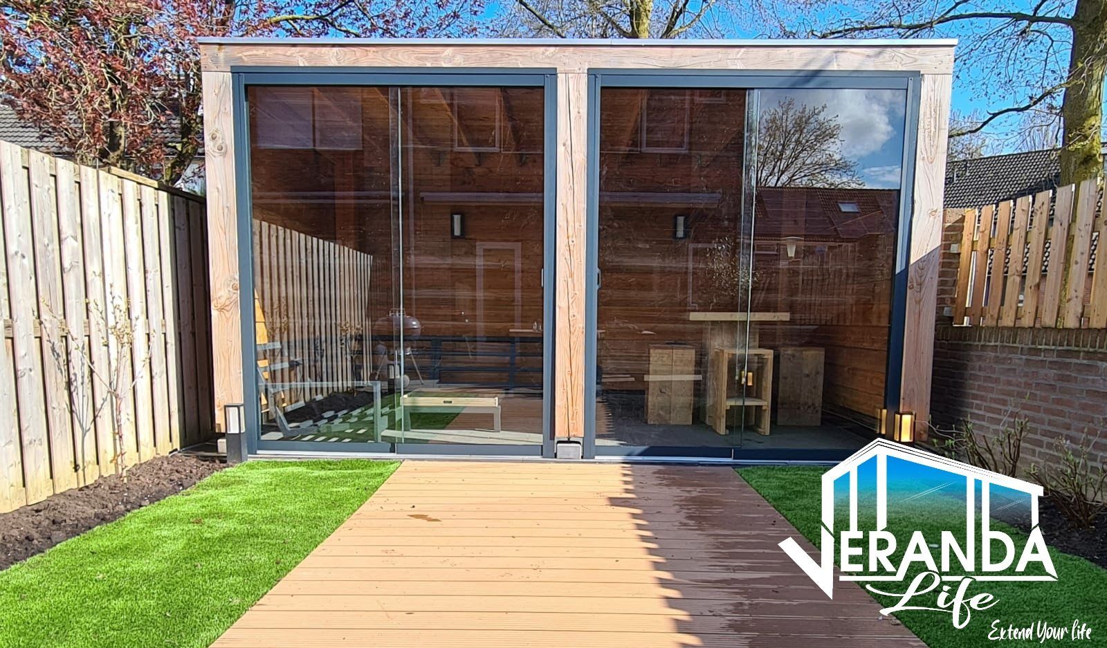 Een houten huis met glazen schuifdeuren in een achtertuin.