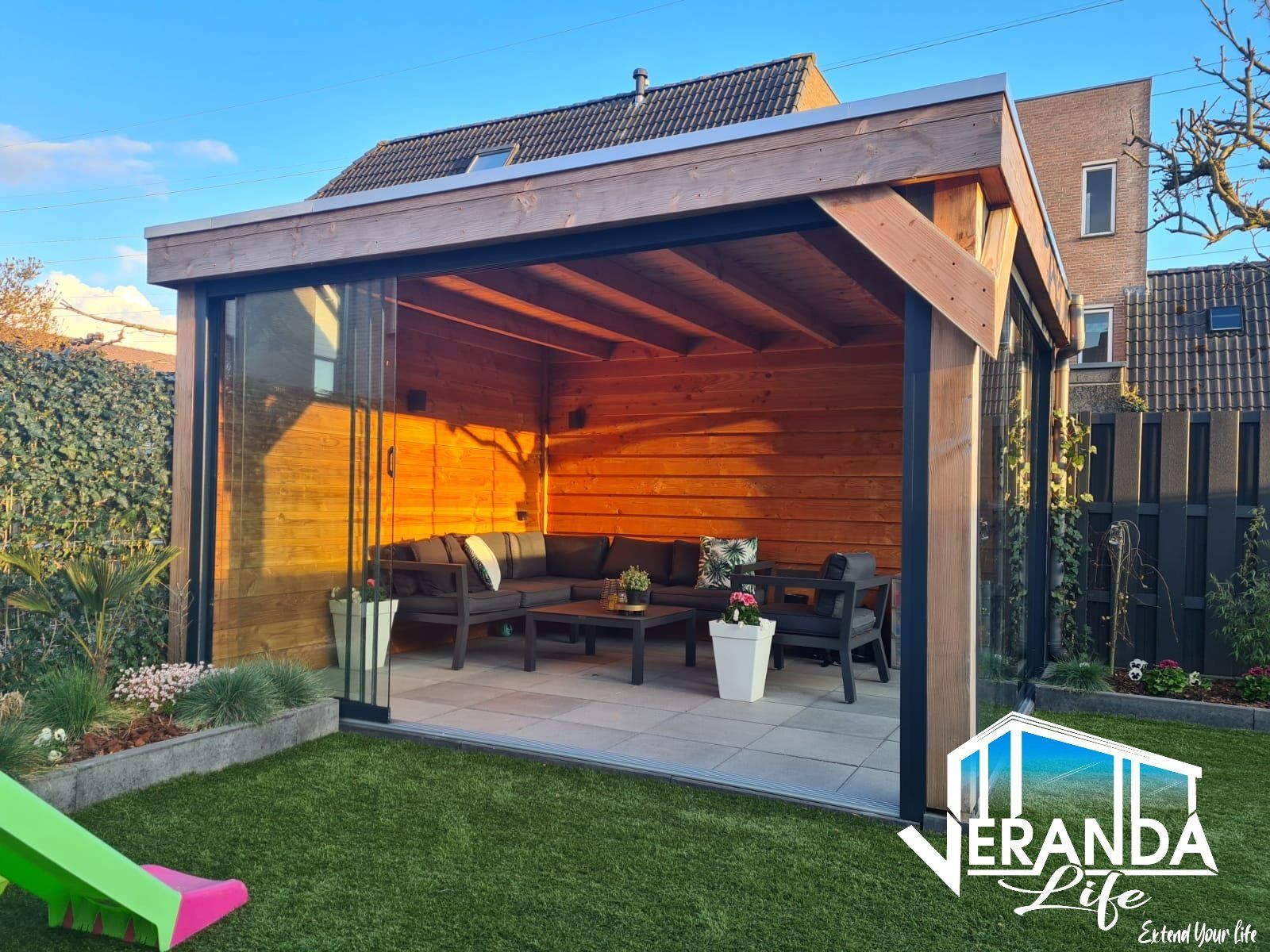 Een houten tuinhuisje met glazen schuifdeuren in een achtertuin.