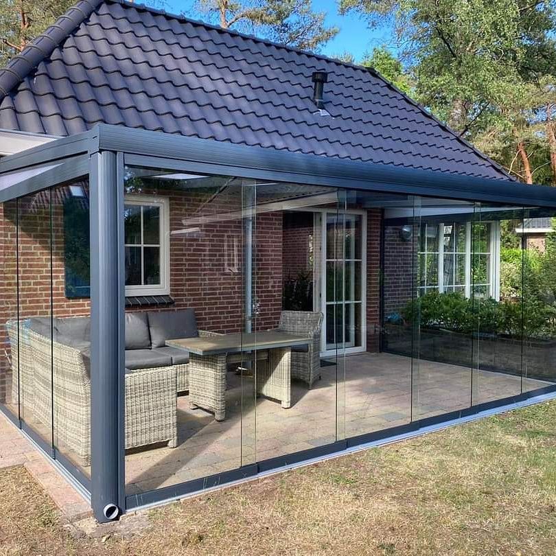 Een bakstenen huis met een met glas overdekt terras met een tafel en stoelen.