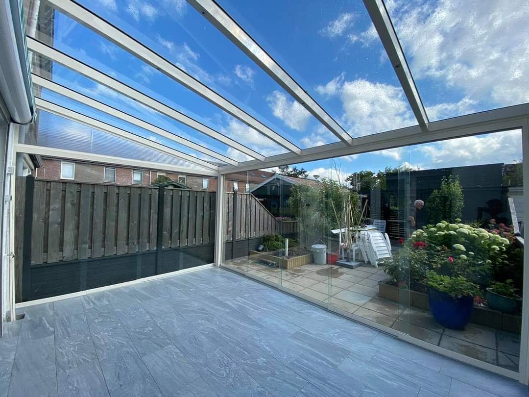 Een groot terras met een glazen dak en een houten hekwerk.