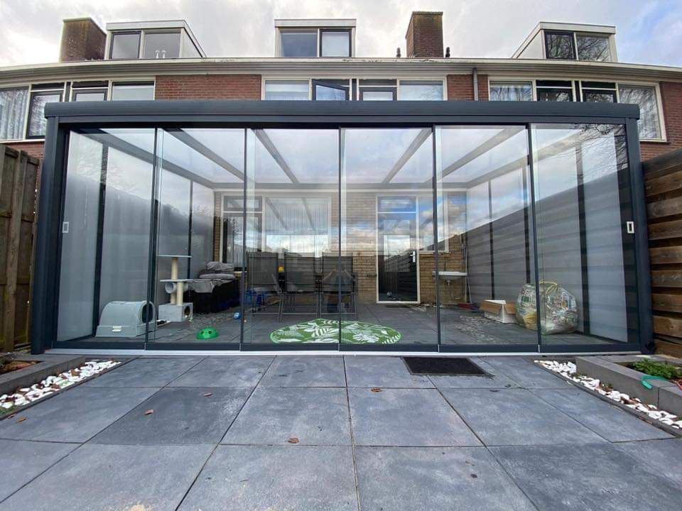 Een grote glazen kamer met glazen schuifdeuren bevindt zich in de achtertuin van een huis.