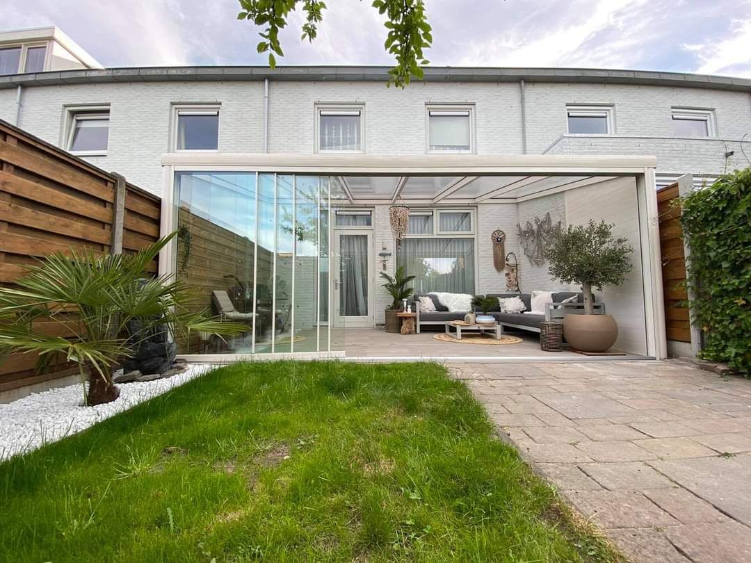 De achtertuin van een huis met een terras en een serre.