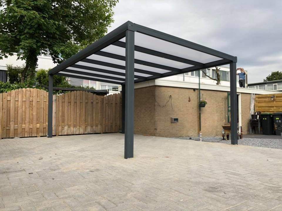 Voor een huis staat een carport met een helder dak.