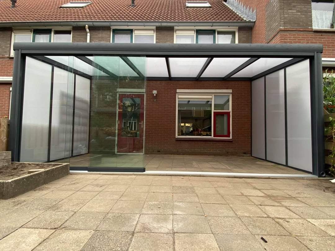Voor een bakstenen huis staat een carport met een glazen dak.