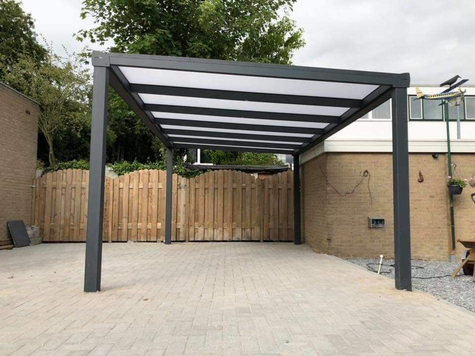 Een carport met een helder dak en een houten hekwerk voor een huis.