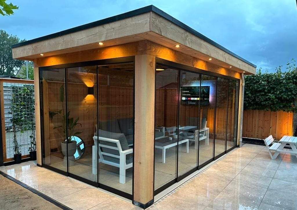 Een houten tuinhuisje met glazen schuifdeuren en een flatscreen tv.