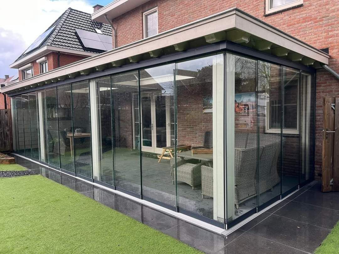 Een grote glazen kamer met een bakstenen huis op de achtergrond.