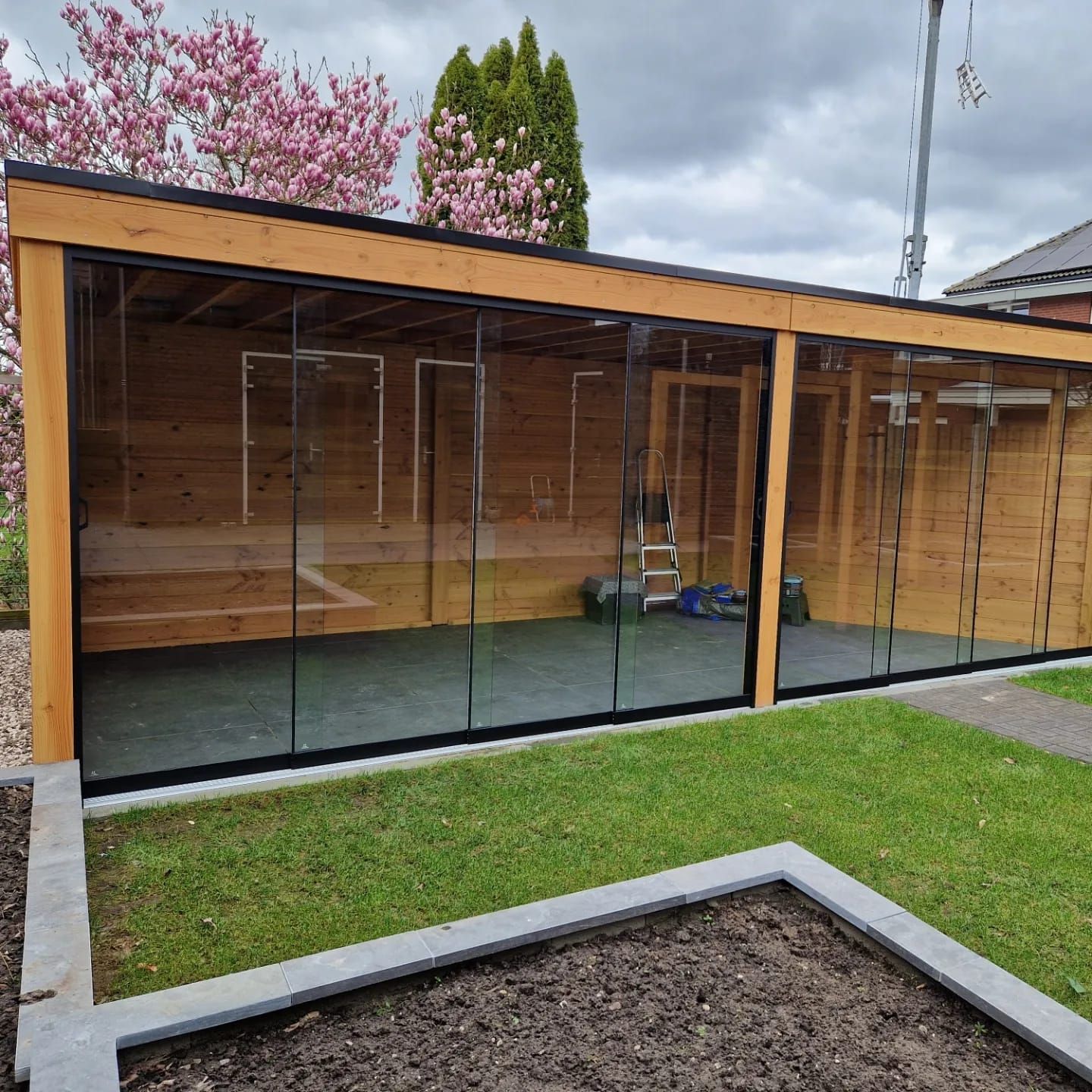 Een houten gebouw met glazen schuifdeuren in een achtertuin.