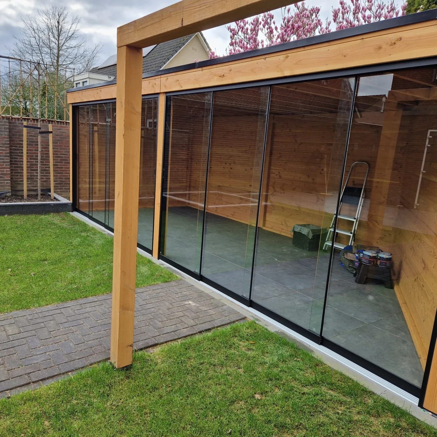 Een houten constructie met glazen schuifdeuren in een achtertuin.