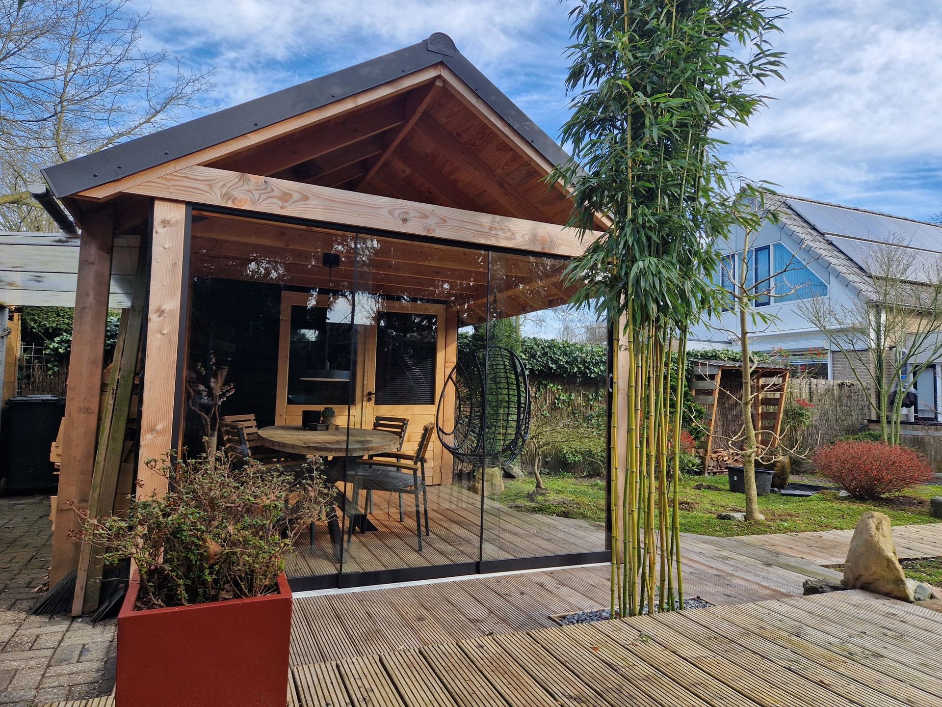 Een houten tuinhuisje met een tafel en stoelen voor een huis.