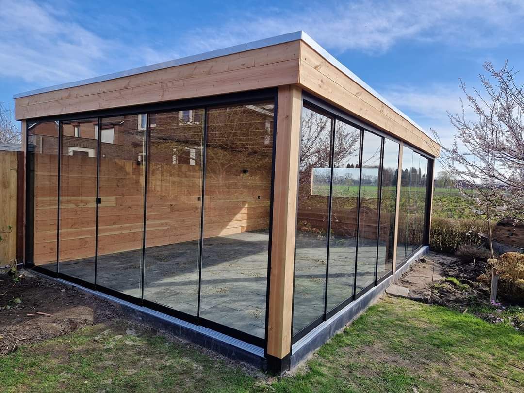 Een houten tuinhuisje met glazen schuifdeuren in een achtertuin.