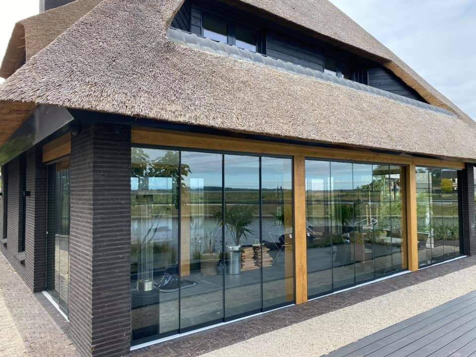 Een huis met een rieten dak en veel ramen