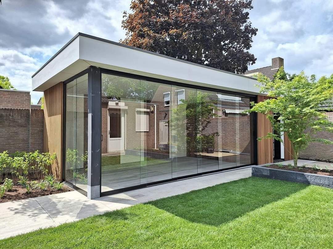 Een klein huis met veel ramen staat op een weelderig groen gazon.