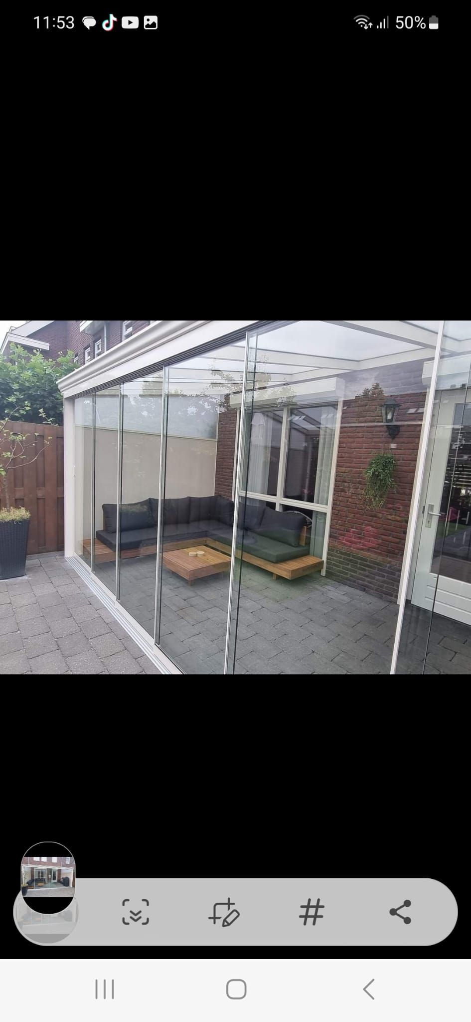 Een terras met een bank en een tafel onder een doorzichtige overkapping.