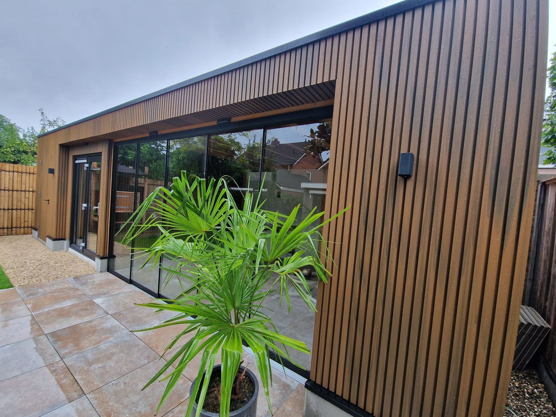Voor een houten gebouw met veel ramen staat een potplant.