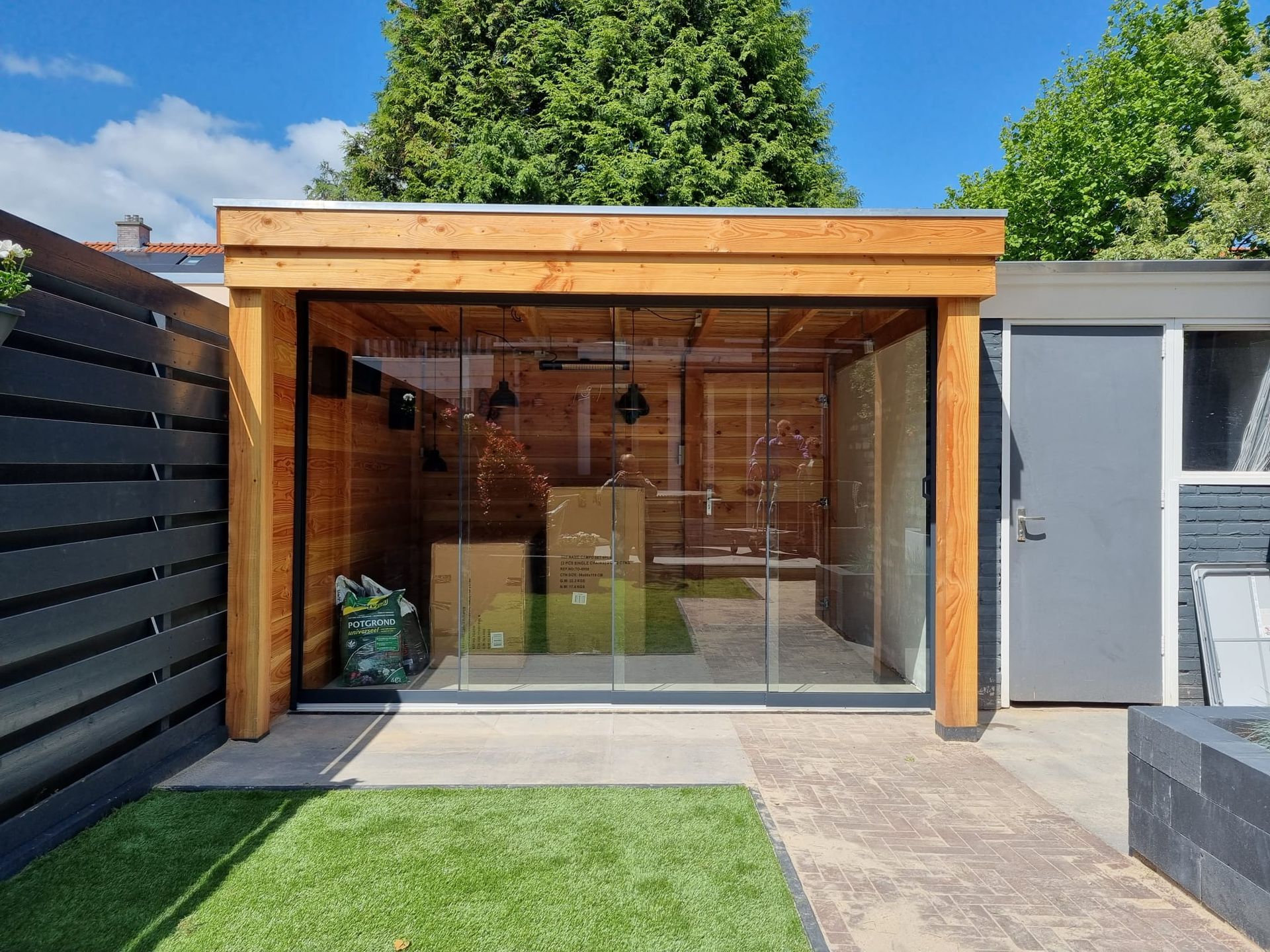 Een houten schuur met glazen schuifdeuren in een achtertuin.