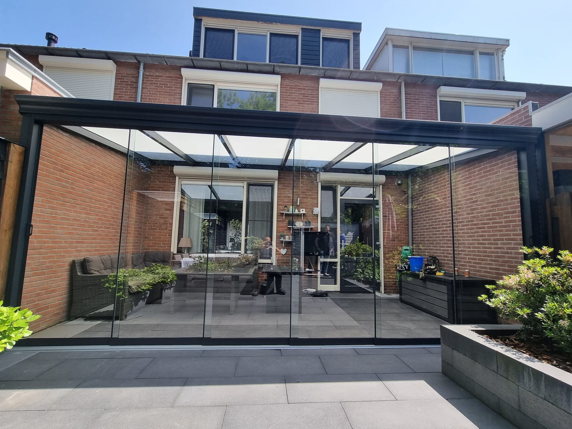 Een bakstenen huis met een met glas overdekt terras ervoor.