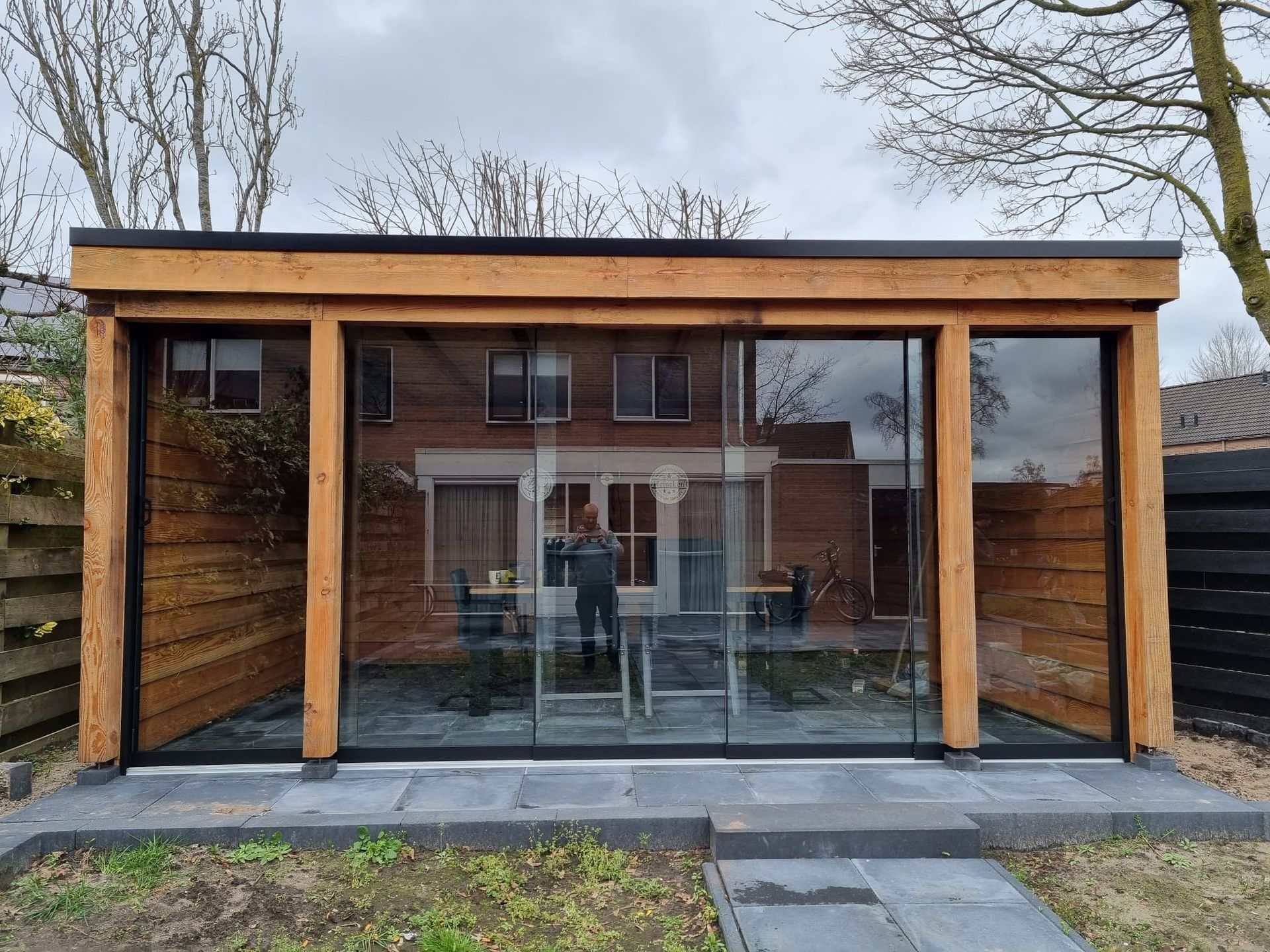 Een houten gebouw met glazen schuifdeuren en een tafel en stoelen binnen.