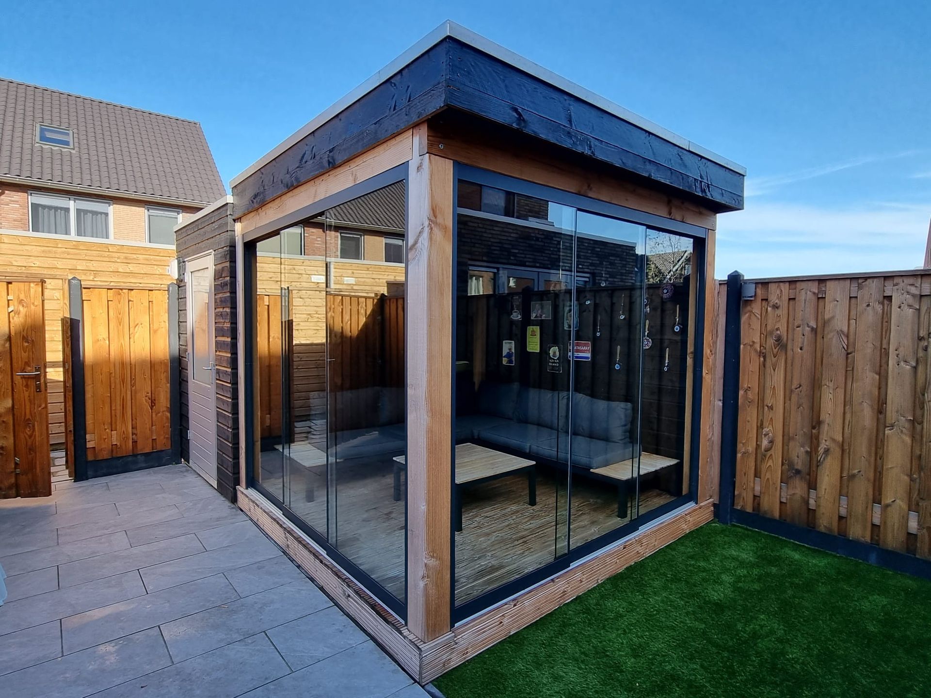 Een houten tuinhuisje met glazen schuifdeuren in een achtertuin.