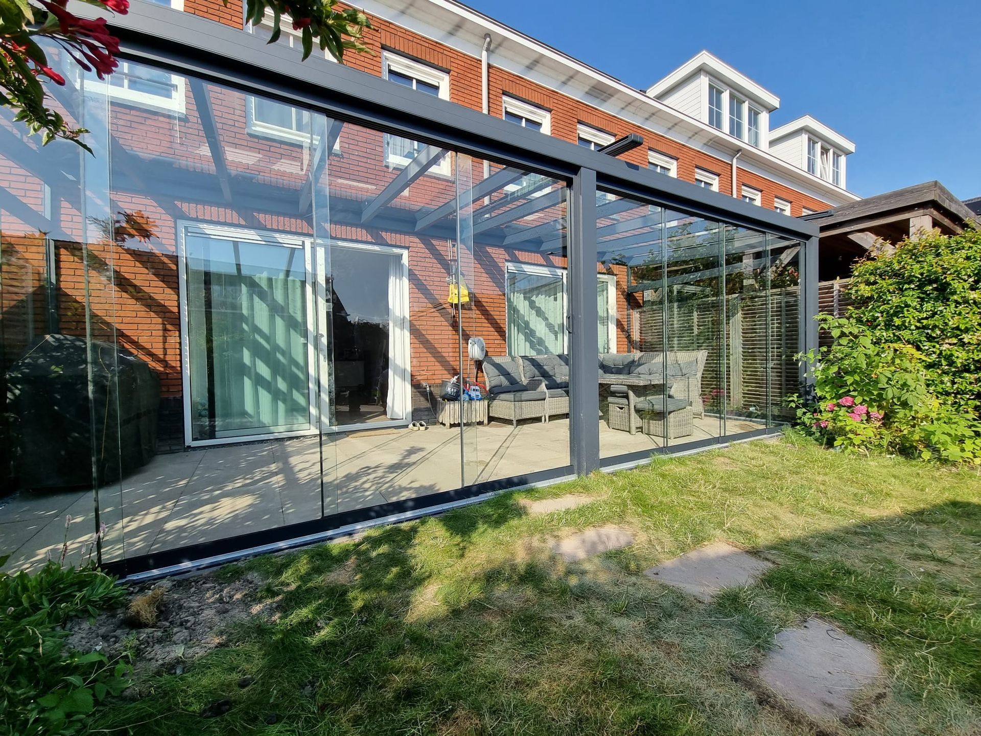 Een glazen pergola met glazen schuifdeuren bevindt zich in de achtertuin van een huis.