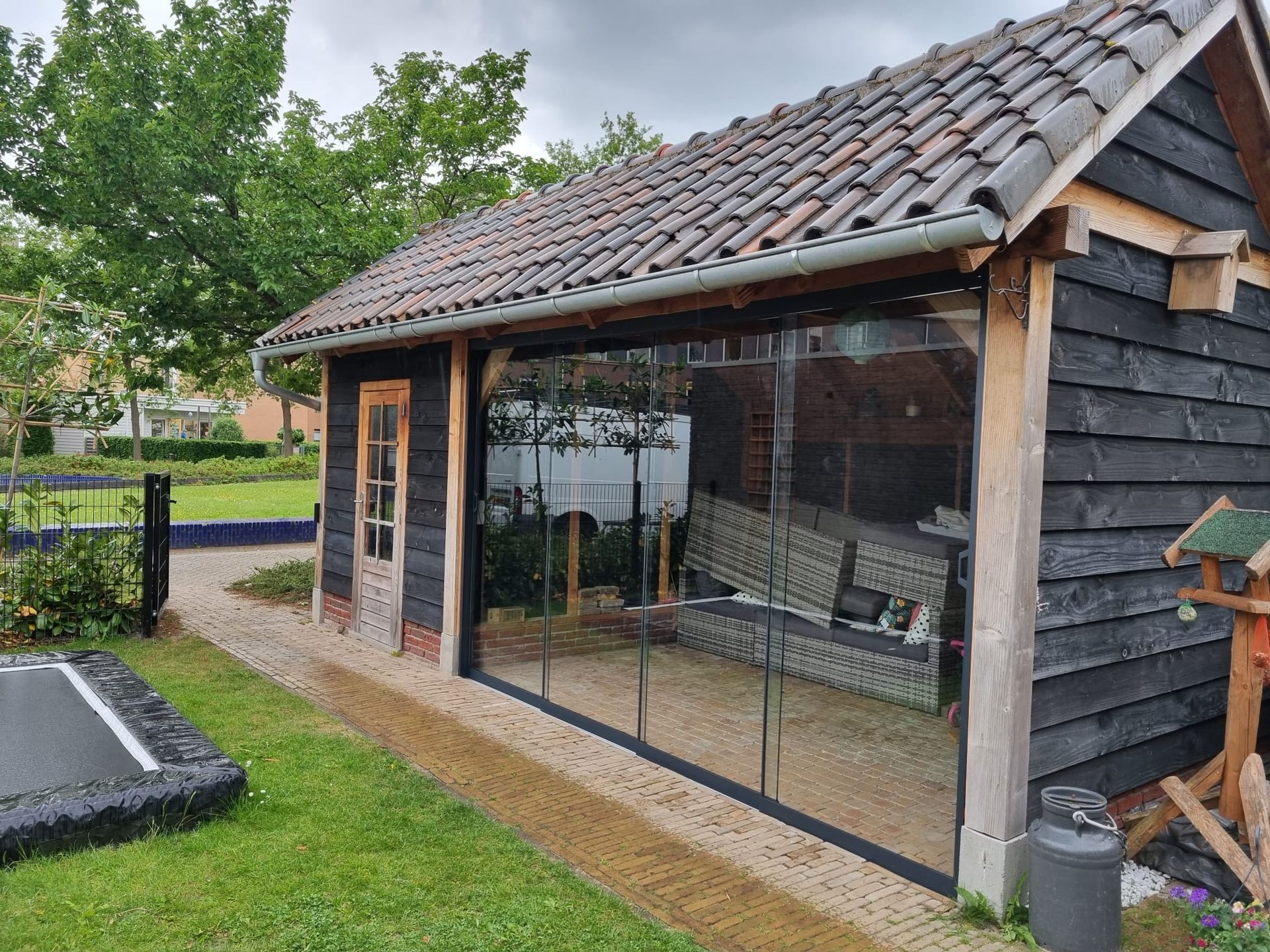 Een zwarte houten schuur met pannendak en glazen schuifdeuren.