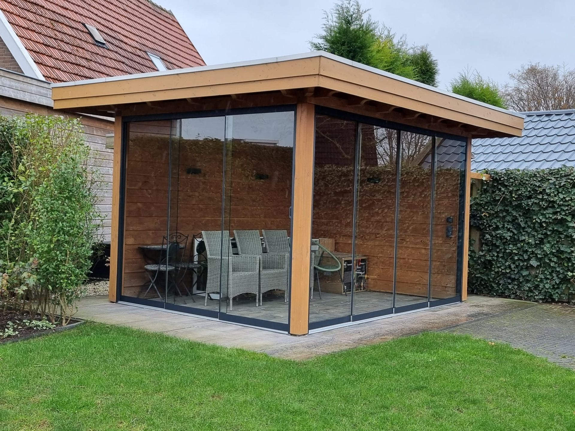 Een houten tuinhuisje met glazen schuifdeuren in een achtertuin.