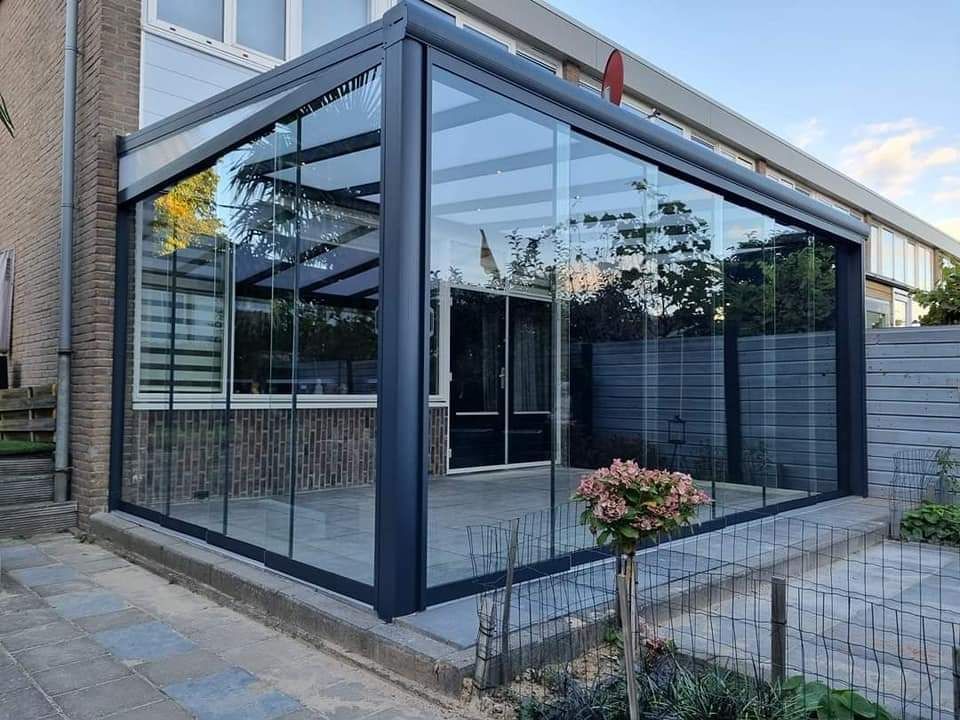 In de zijkant van een huis is een grote glazen kamer met glazen schuifdeuren ingebouwd.