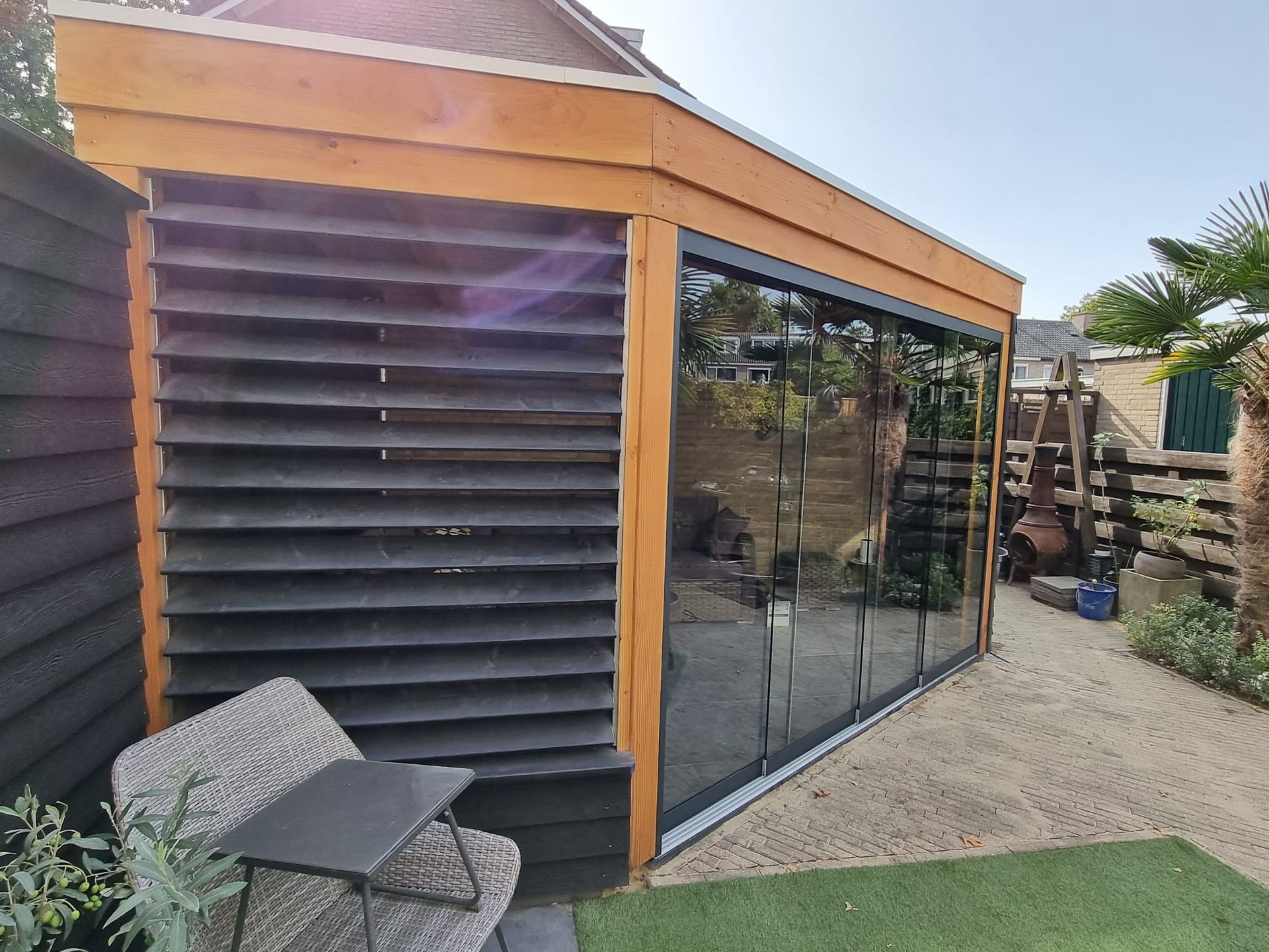 Een houten tuinhuisje met glazen schuifdeuren in een achtertuin.