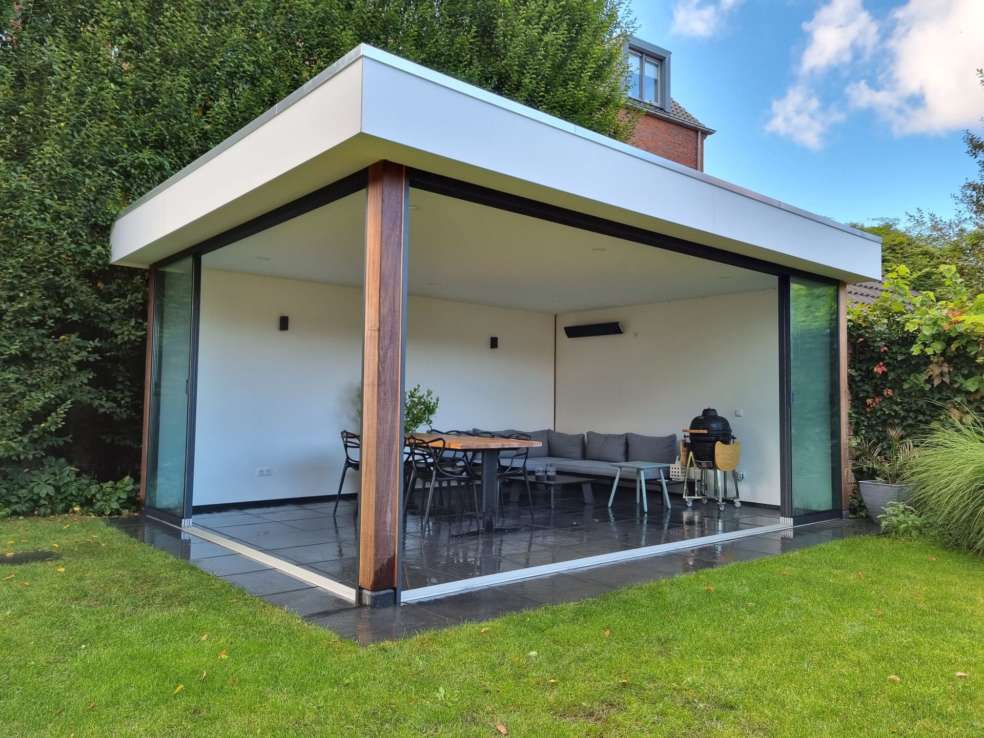 Een groot overdekt terras met een tafel en stoelen in een achtertuin.