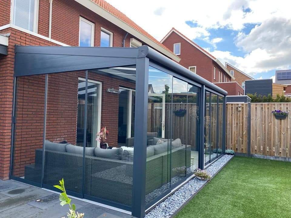 In de achtertuin van een huis staat een pergola met glazen schuifdeuren.
