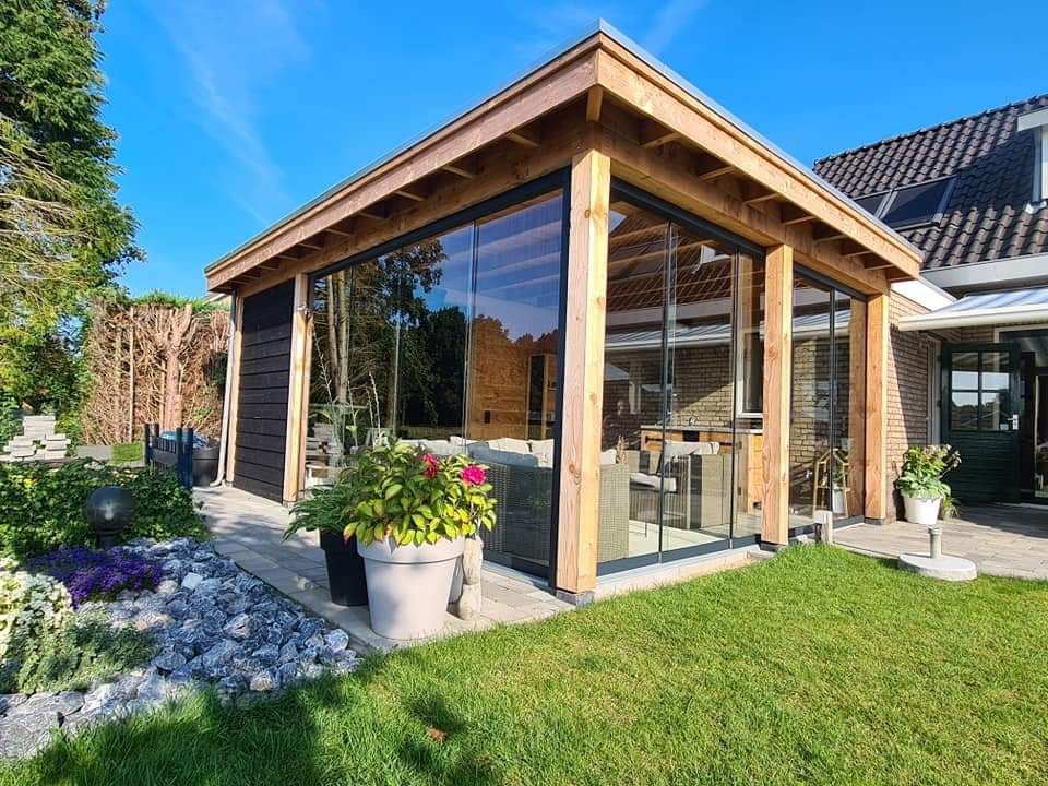 In de achtertuin van een huis staat een houten tuinhuisje met glazen schuifdeuren.