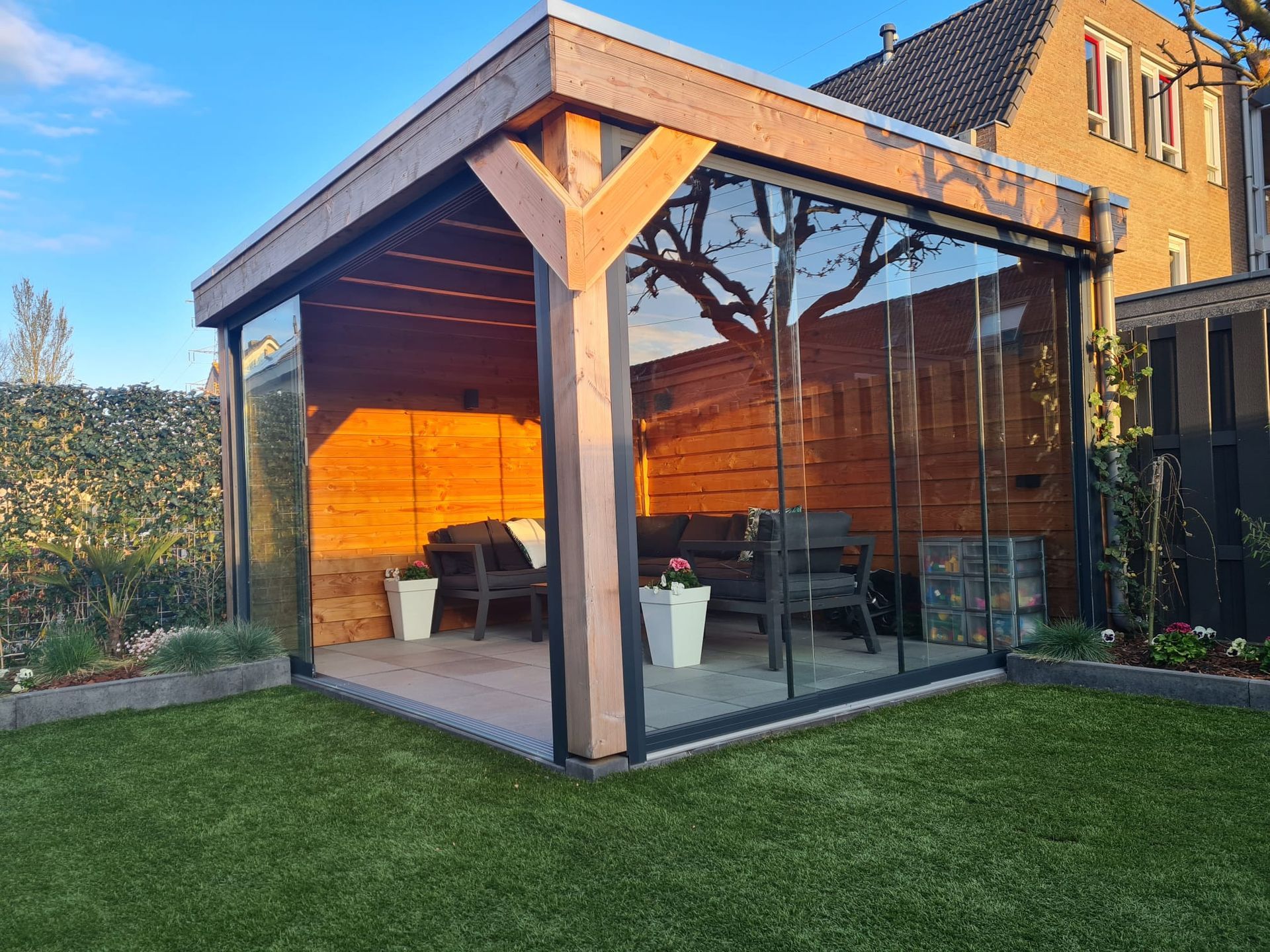 Een houten tuinhuisje met glazen schuifdeuren in een achtertuin.