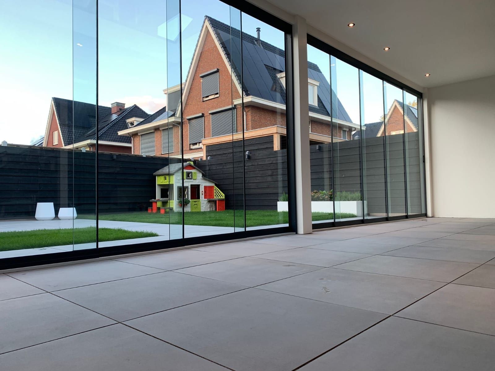 Een lege kamer met veel ramen en een huis op de achtergrond.