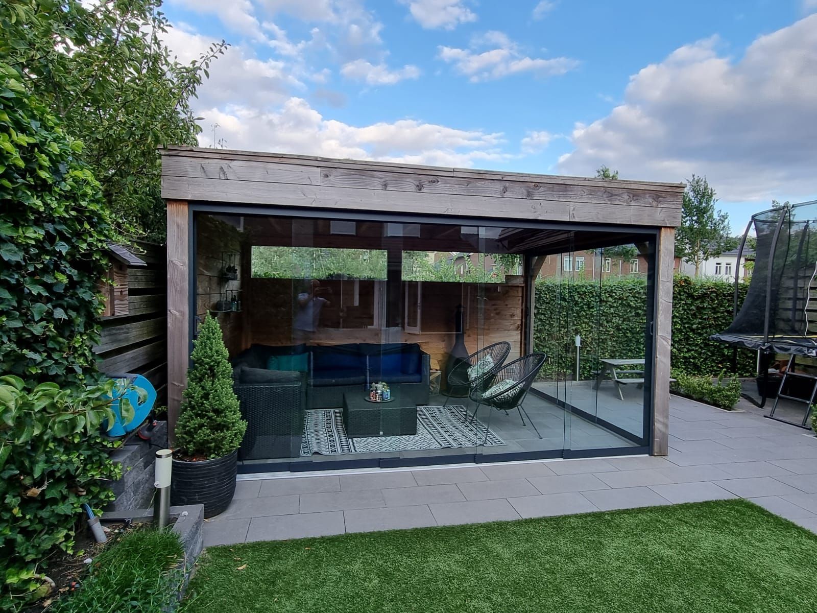 Een houten tuinhuisje met glazen schuifdeuren in een achtertuin.