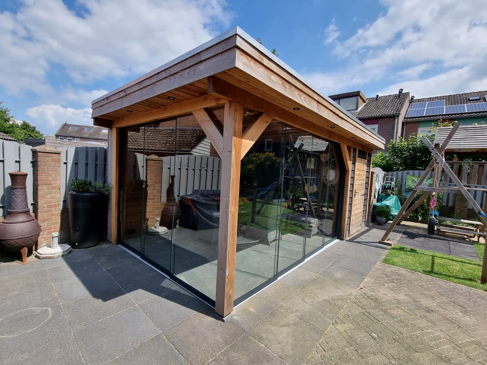 Een houten tuinhuisje met glazen schuifdeuren in een achtertuin.