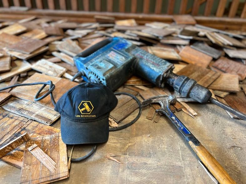 A hat , hammer , and drill are on a pile of wood.