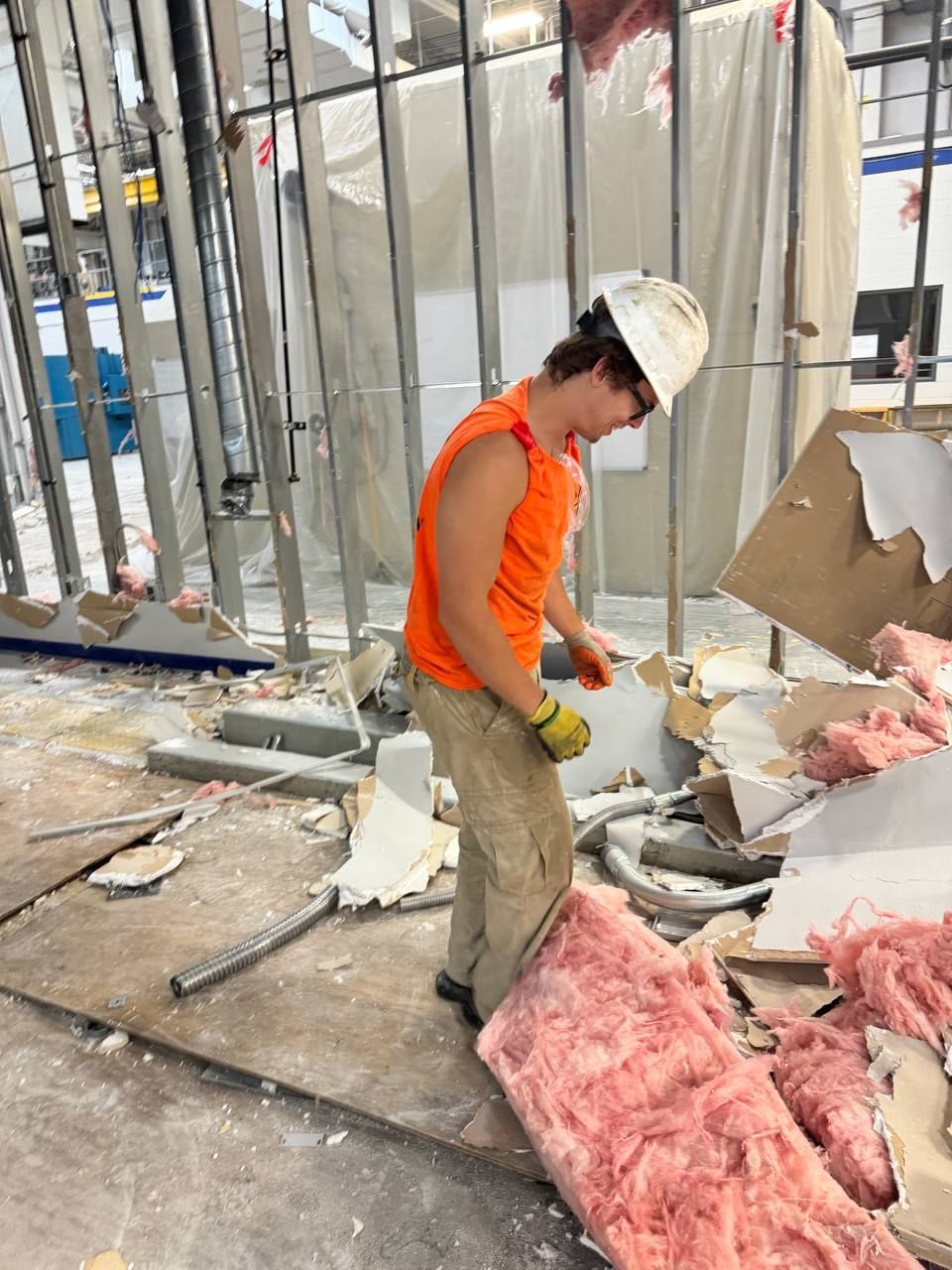 A man wearing a hard hat is standing in a room with pink insulation.