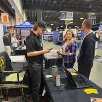 A group of people are standing around a table at a convention.
