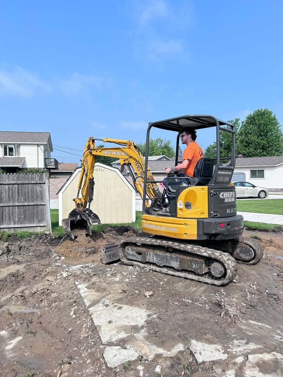 A man is driving a small yellow excavator on a dirt road.