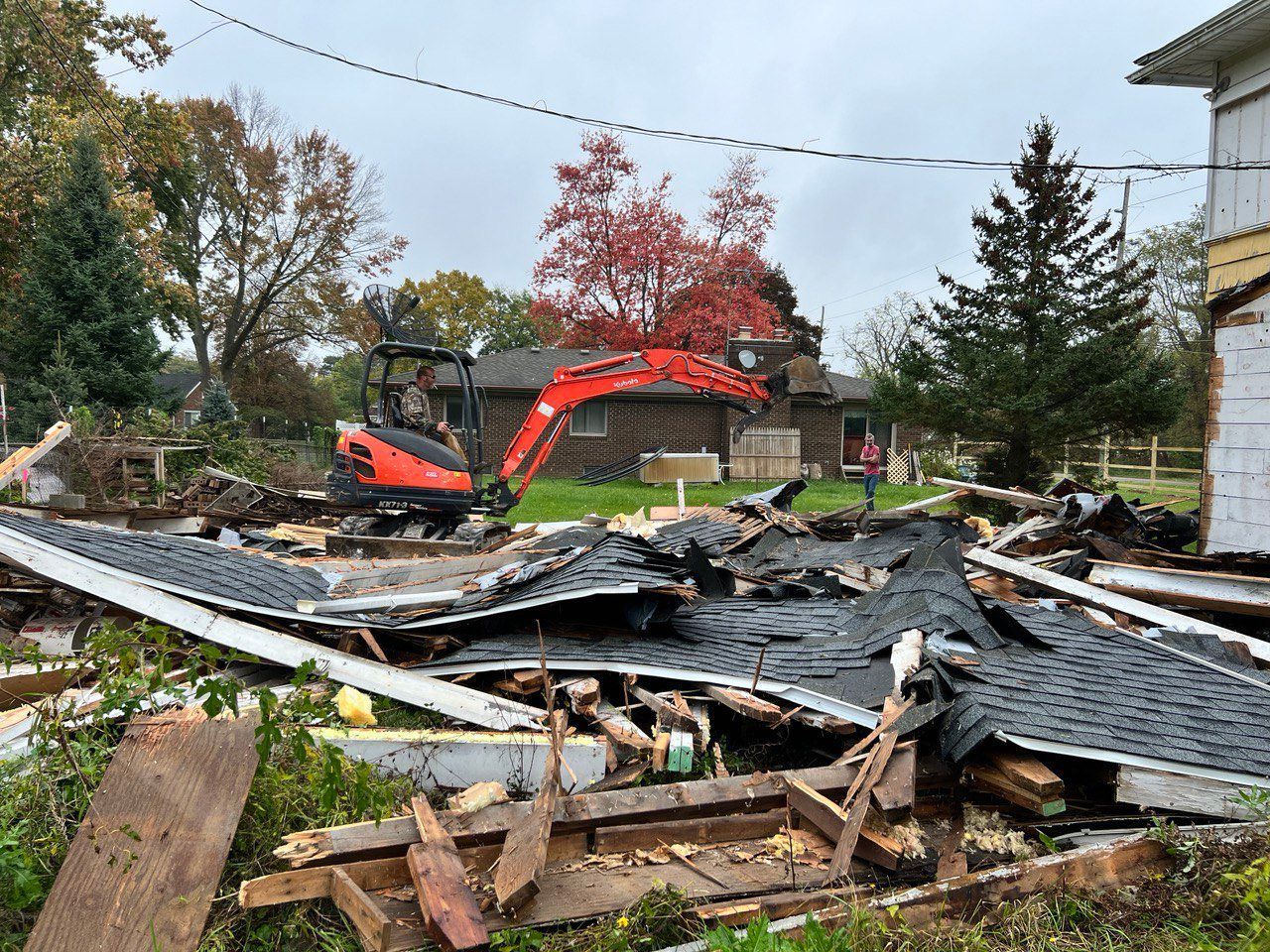 A house is being demolished with a bulldozer in the background.
